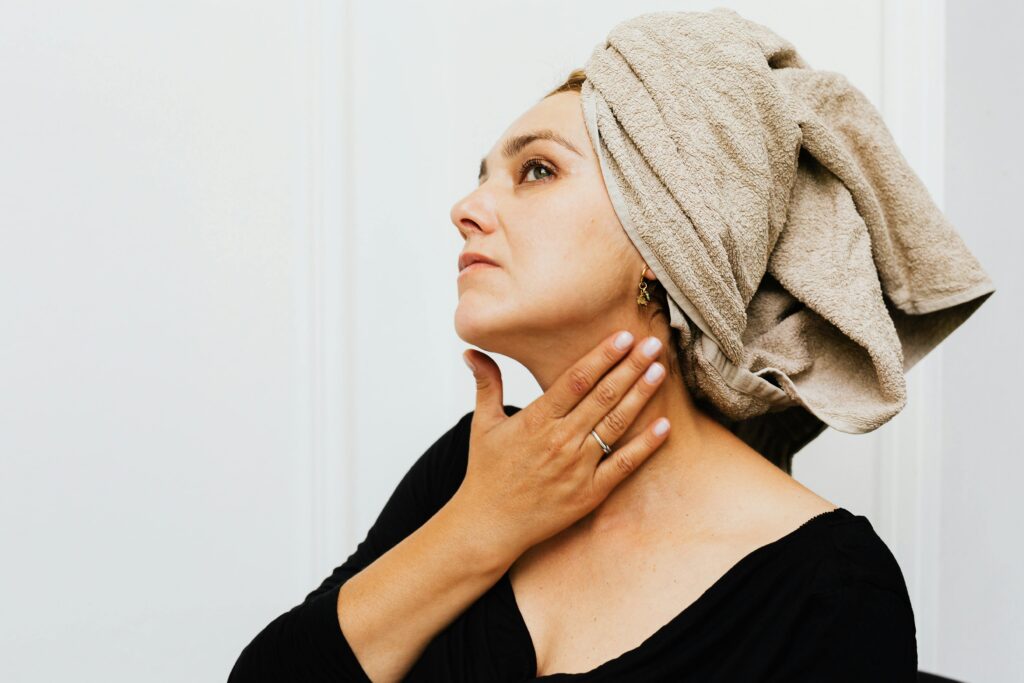 Woman with towel wrapped hair applying skincare cream indoors.