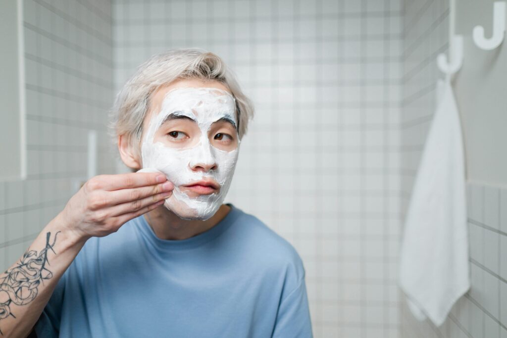A young man in a bathroom applies a skincare mask to maintain healthy skin.